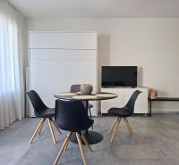Dining area with a television and a table in a 2-room apartment with a wooden decor floor.