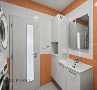 A bathroom in a 2-room apartment with a washing machine, dryer, and sink, white with orange elements.