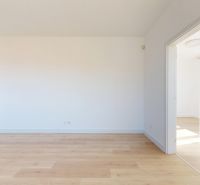 An empty room in a 3-room apartment with a wood-patterned floor and white walls.