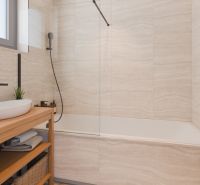 A bathroom in a family house with a bathtub, wooden shelf, and window.