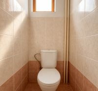 A toilet in a cabin with ceramic tiles and a small window.