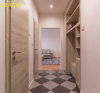 A hallway with checkerboard flooring, built-in shelves, and a view into the living room in a 2-room apartment.