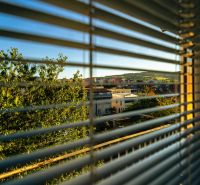 A view through the blinds of Bardejov from Fučíkova Street, overlooking greenery and buildings.