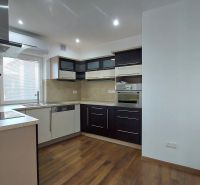 A kitchen in a 2-room apartment with dark furniture and a wooden decor floor.