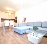 A bright living room of a two-room apartment with a wooden decor floor and a gray sofa.