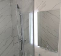 A bathroom with marble-look tiles and a shower in a 3-room apartment.