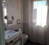 Bathroom in the villa with a sink, toilet, and a window with a curtain.