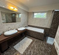 A bathroom in a family house with a shower, a bathtub, a double sink, and marble walls.