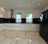 A kitchen with black and white cabinets, a black refrigerator, and ceramic flooring.