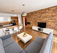Living room of a two-room apartment with a wooden decor floor and a brick wall.