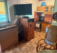 Interior of a cottage with a television, kitchen unit, stove, and comfortable armchair.
