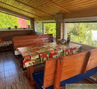A wooden interior of a cabin with seating, a table, and a view of nature.