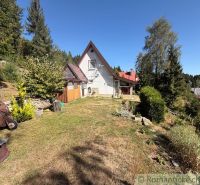 A cottage in Látky surrounded by greenery and trees, a stone courtyard, and a pleasant environment.
