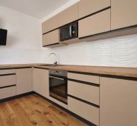 A kitchen in a 2-room apartment with a wooden decor floor and light cabinets.