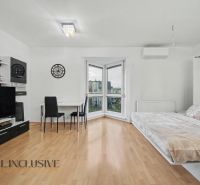 Living room with wood-patterned flooring, a bed, and a table in a studio apartment.