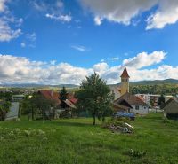 A view of family houses in the village of Banka, Topoľčianska Street with a church in the background.