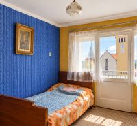 A room in a family house with a bed, blue wallpaper, and a view of the church.