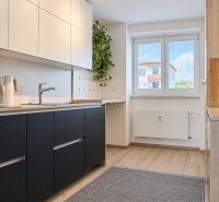 A kitchen in a 3-room apartment with a wooden decor floor and white cabinets.