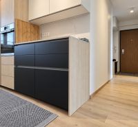 A kitchen in a 3-room apartment with a wooden decor floor and black cabinets.