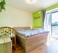 A bedroom in a 3-room apartment with a bed, a baby crib, and a floor with a wooden decor.