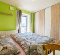 Bedroom in a 3-room apartment with a green wall, floral bedding, and a wardrobe.