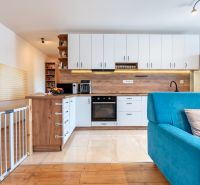 A kitchen in a 3-room apartment with white cabinets, a blue sofa, and a floor with a wooden decor.