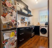 A kitchen in a 3-room apartment with a wooden decor floor and black furniture.
