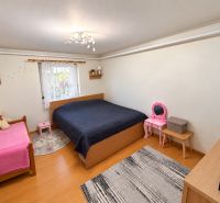 A bedroom with wood-patterned flooring, two beds, and children's furniture in a studio apartment.