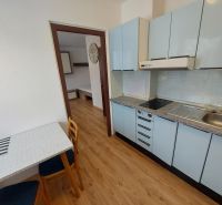 A kitchen with blue cabinets, a wooden decor floor, and a dining table in a studio apartment.