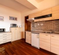 The kitchen of a 2-room apartment with a wooden decor floor and light furniture.