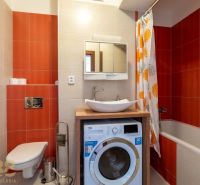 A bathroom in a 2-room apartment with a washing machine, a bathtub, and orange tiles.