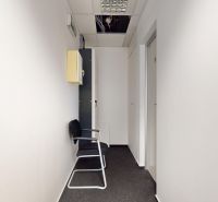 A narrow office corridor with white walls, a black office chair, and a suspended ceiling.