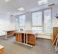 An office with wooden decor, large windows, and carpet, equipped with desks and coat racks.