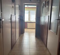A hallway in a family house with tiles, lined with walls, leading to windows with blinds.