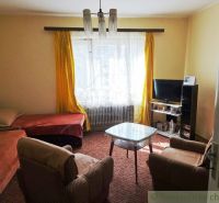 A living room in a family house with a bed and a television, yellow curtains.