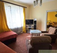 A living room of a family house with carpets, armchairs, and yellow curtains.