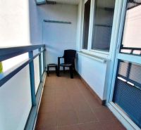 A balcony in a studio apartment with a plastic chair and tiles on the floor.