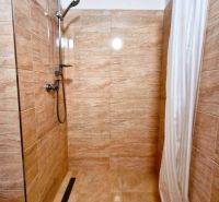 A shower corner with beige tiles in a studio apartment.