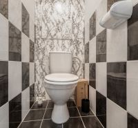 A toilet with black and white wall tiles in a 4-room apartment.