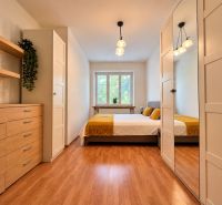A bedroom in a 2-room apartment with a wood-patterned floor and modern furniture.