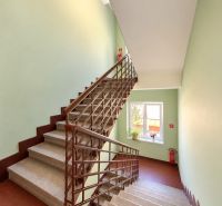 A staircase in a 2-room apartment with a room window, light-colored walls, and a fire extinguisher.