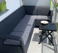 A balcony in a 2-room apartment with a rattan sofa and a small table.