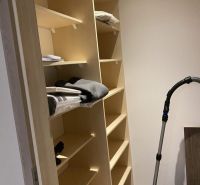 A storage unit with shelves, in the corner of the room, next to a vacuum cleaner.