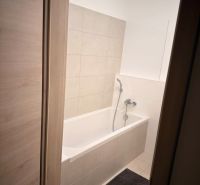 A bathroom with a bathtub and beige tiles in a 2-room apartment.