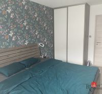 A bedroom with floral wallpaper, a double bed, a wardrobe, and composite flooring.
