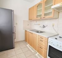 A kitchen in a studio apartment with a refrigerator, stove, and light-colored furniture.
