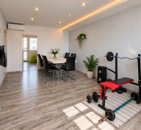 Dining room in a 4-room apartment with a table, a workout bench, and a wooden-patterned floor.