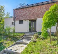 A family house in Vtáčie údolie, Bratislava - Koliba, surrounded by greenery and a paved walkway.