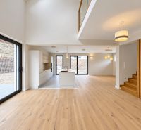 Open space in a family house with a kitchen, large windows, and wooden decor flooring.