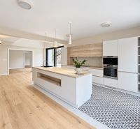 A kitchen in a family house with an island, white cabinets, and a wood-patterned floor.